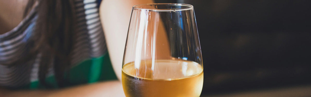 Ein Glas Weißwein vor einer Person im Hintergrund