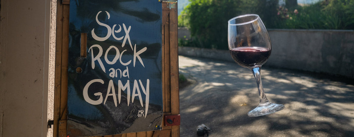 Ein Schild mit der Aufschrift Sex Rock and Gamay neben einem Glas Rotwein im Freien.